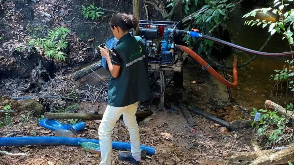 Mulher utilizando o celular para realizar teste de vazão perto de equipamento de coleta de recurso hídrico e próximo do rio