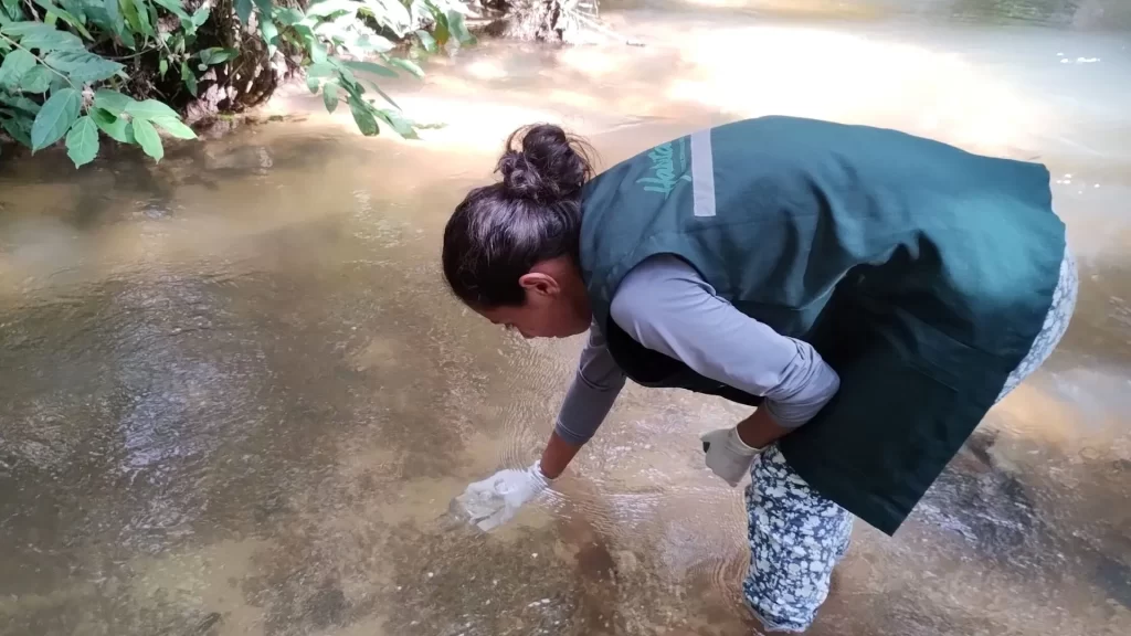 Geografa agachada coletando recurso hídrico em rio para análise