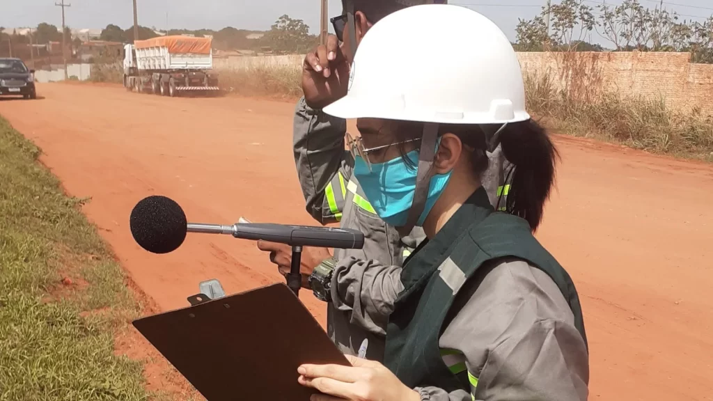 Duas pessoas no exterior da indústria de fertilizante realizando o monitoramento de ruído ambiental.