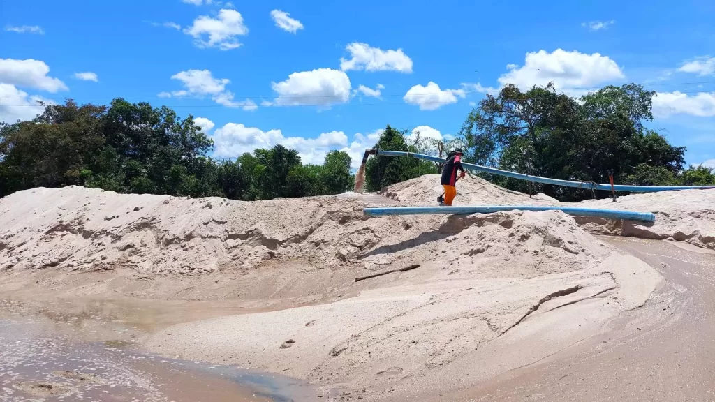 Área de mineração com areia na coloração branca com trabalhador em cima do minério. 