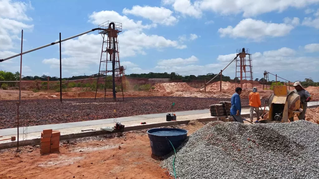 Vista de área de mineradora realizando a extração de argila, e três funcionários ao lado direito da foto trabalhando na produção de cascalho.